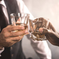 Close up partial view of two men in formal wear clinking whiskey