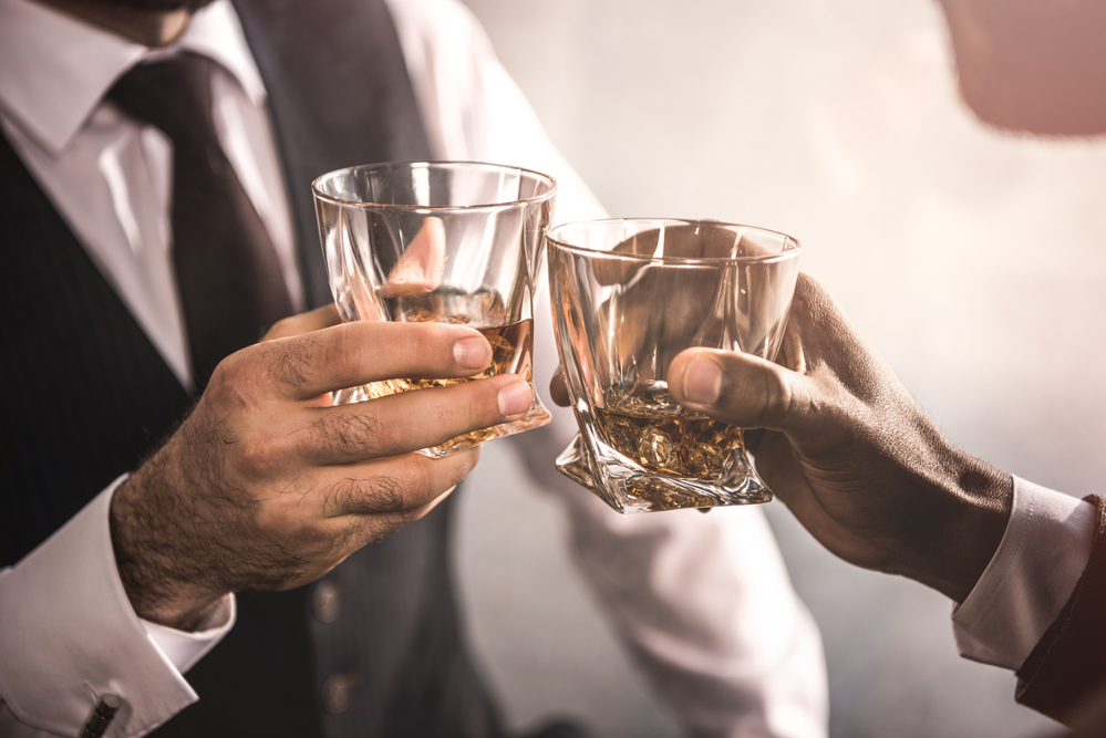 Close up partial view of two men in formal wear clinking whiskey