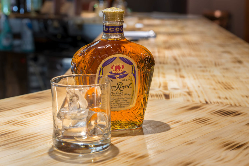 Crown Royal whiskey on a table, next to a glass with ice - The Flask and Barrel