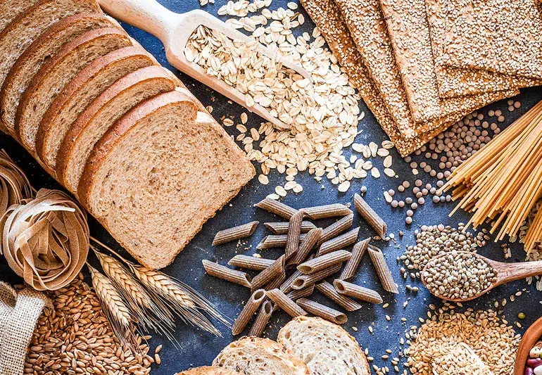 Assorted whole grains, bread, and pasta on dark surface.