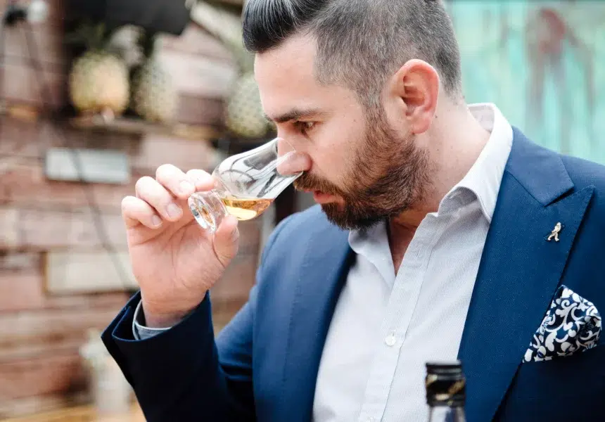 Man nosing whiskey in suit outdoors.