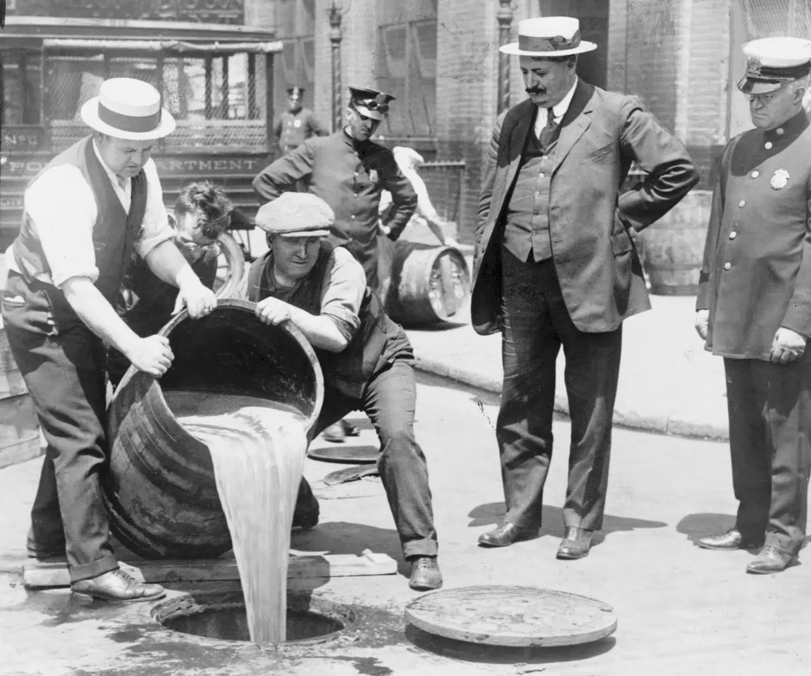 Men pouring liquid into sewer during Prohibition era.