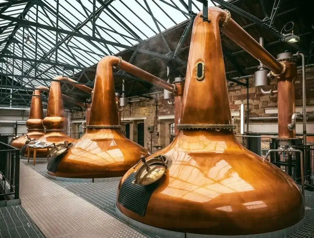 Copper whisky distillery stills in industrial setting.