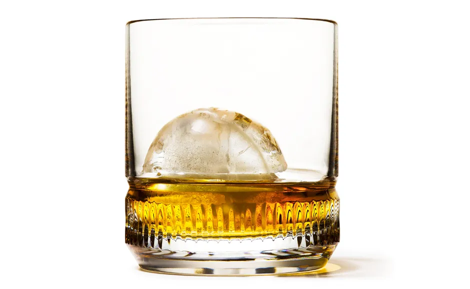 Whiskey glass with ice ball on white background.