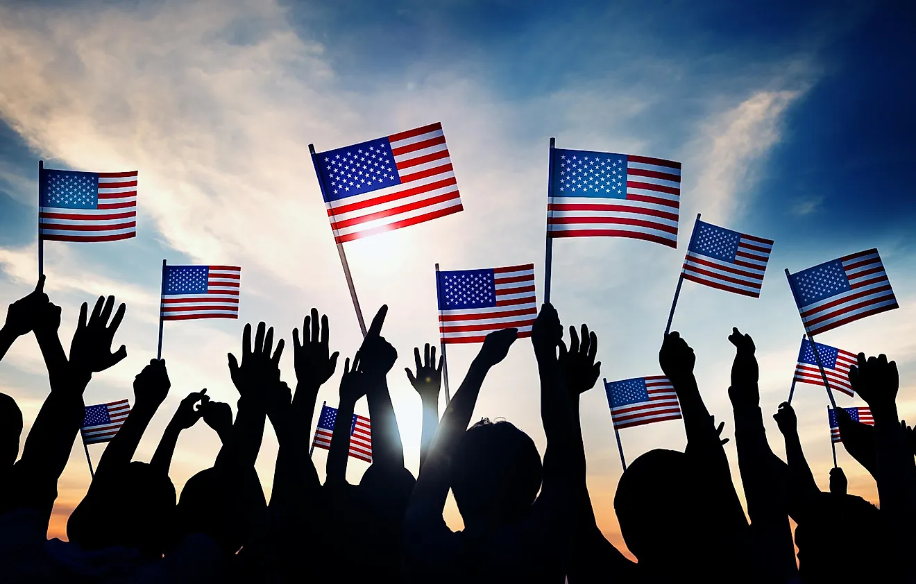 People waving American flags against sunset sky.