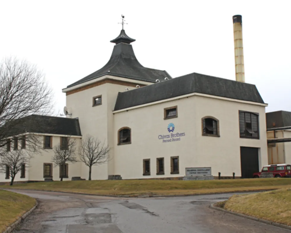 Historic distillery building with large chimney and logo.