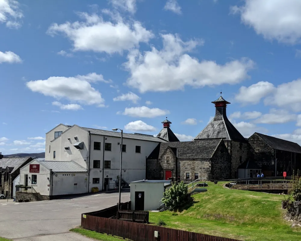 Historic distillery buildings under blue sky with clouds.