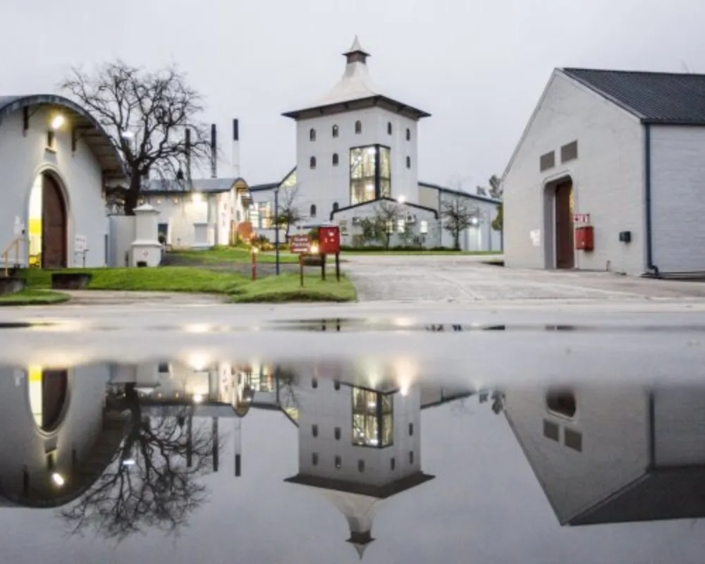 Historic distillery buildings reflected in water after rain.
