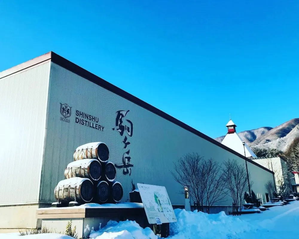 Shinshu Distillery exterior with whiskey barrels in snow.