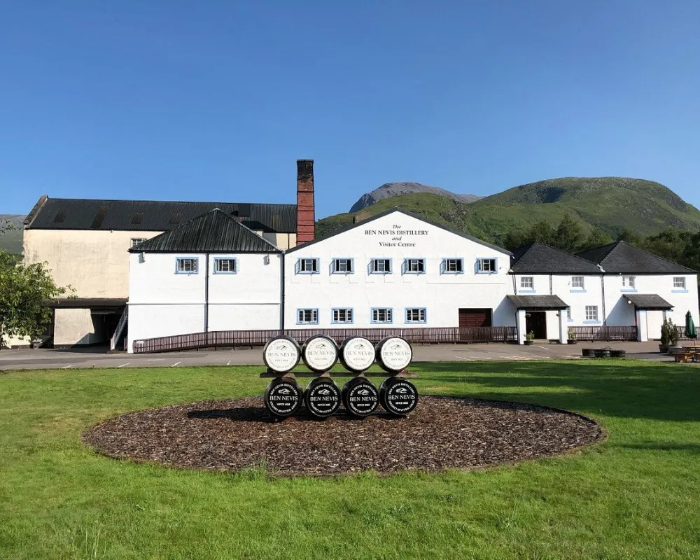 Ben Nevis Distillery with casks and mountain background.