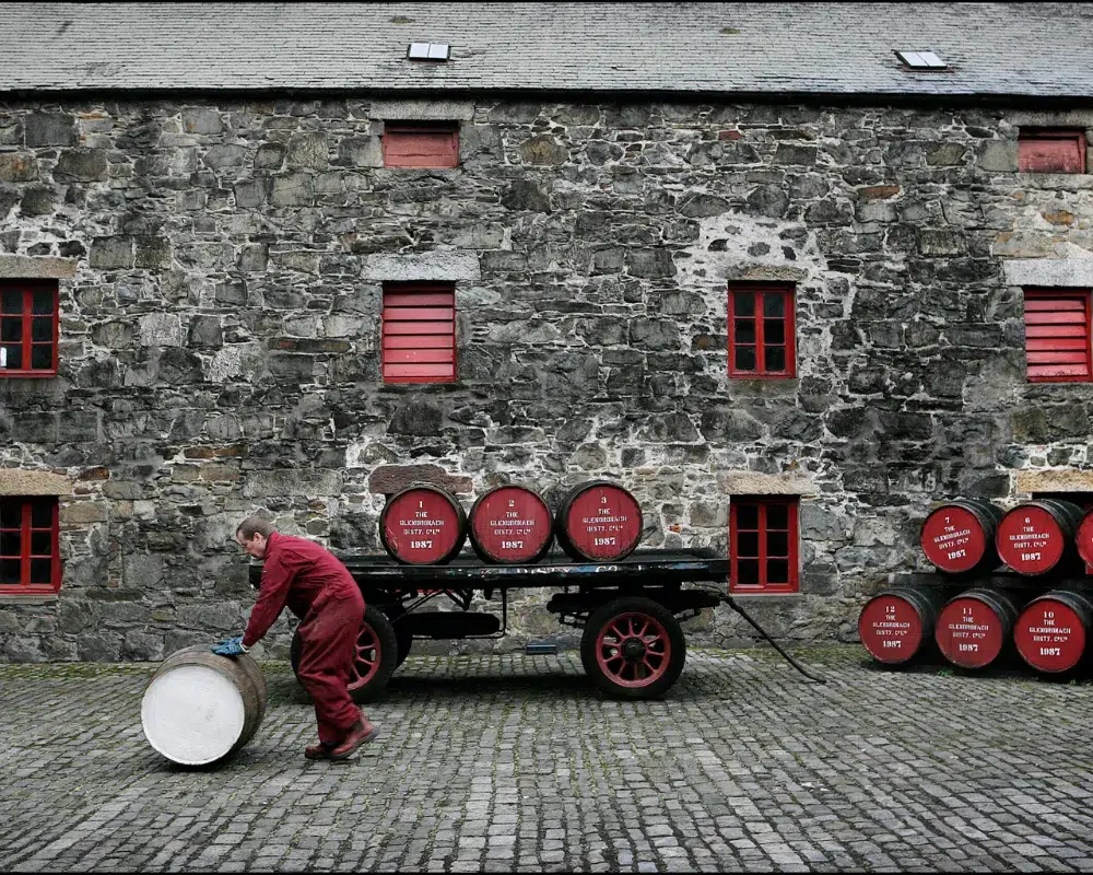 Worker rolling barrel by historic distillery building.