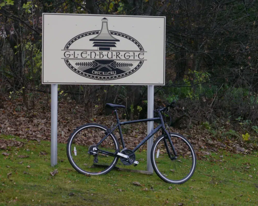 Bicycle parked by Glenburgie Distillery sign outdoors.