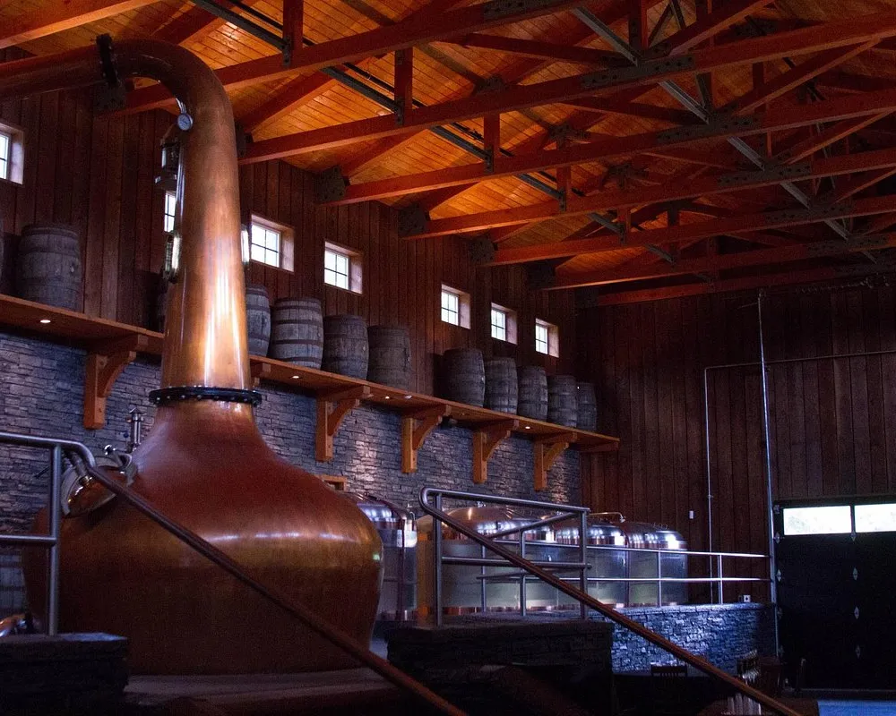 Copper whiskey distillery equipment with barrels in background.