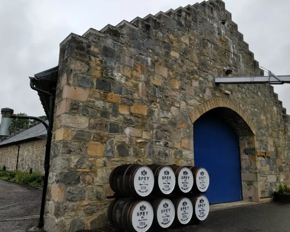 Distillery entrance with whiskey barrels and stone facade.