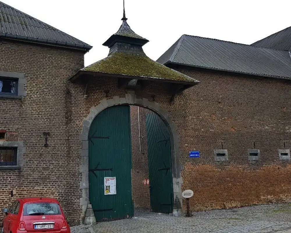 Historic brick building with moss-covered gate and small car.