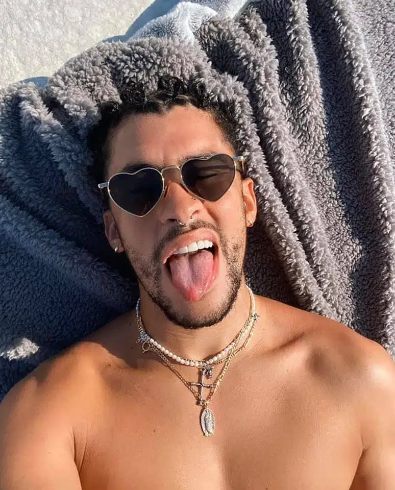 Man with sunglasses sticking out tongue, wearing necklaces.