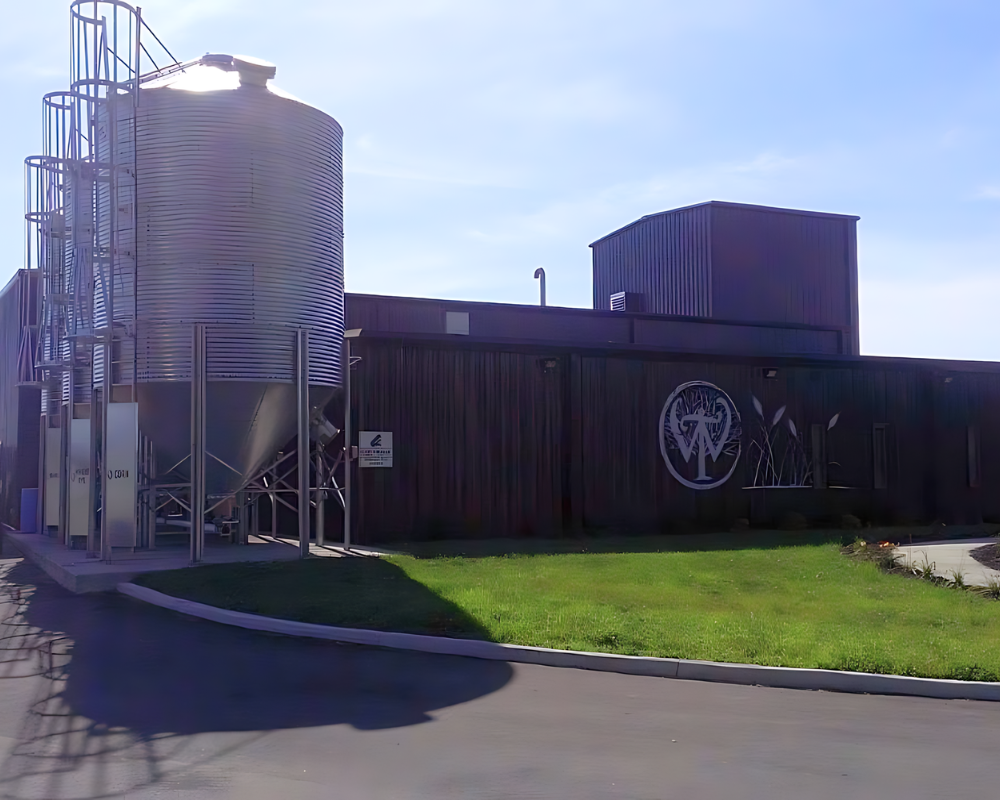 Modern brewery building with large silo and company logo.