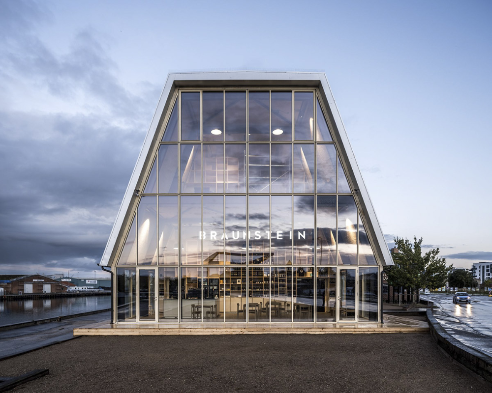 Modern glass building by water at dusk.