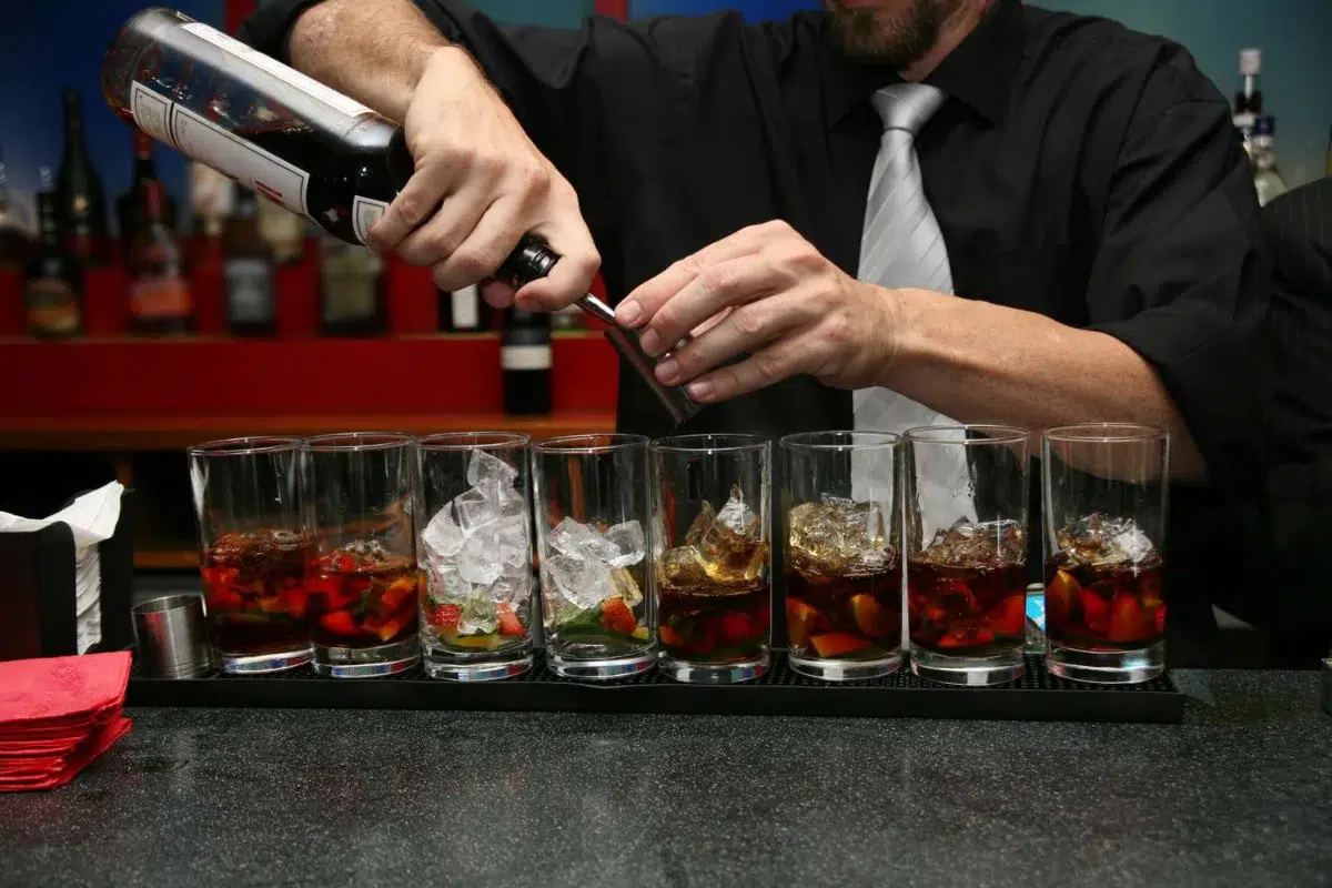 Bartender pouring drinks into glasses with ice.