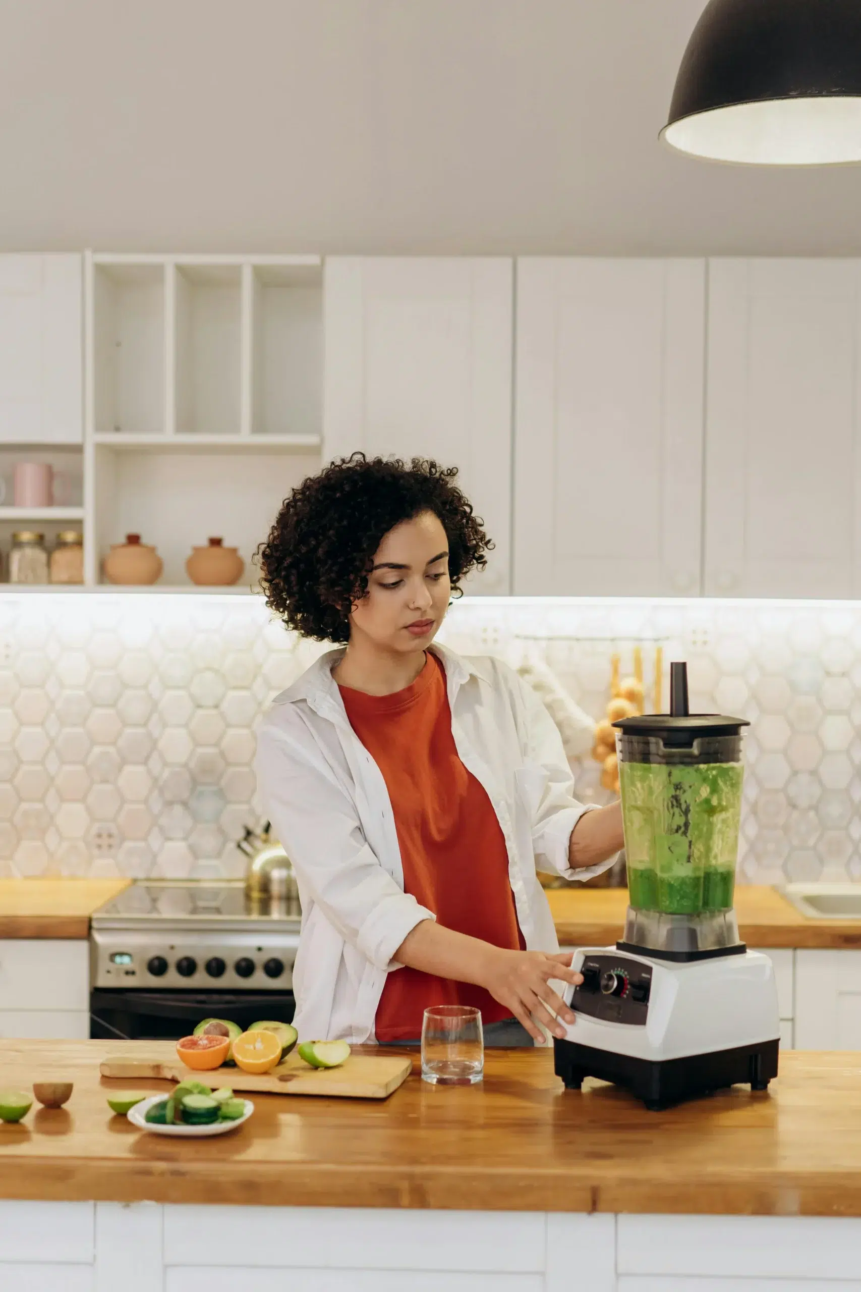 Woman using blender with fresh ingredients in kitchen.