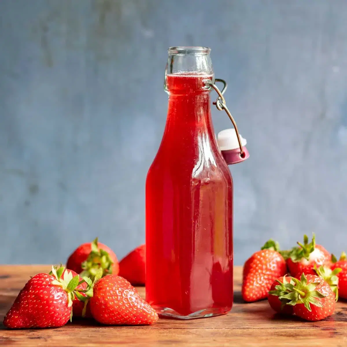 Strawberry syrup in glass bottle with fresh strawberries.