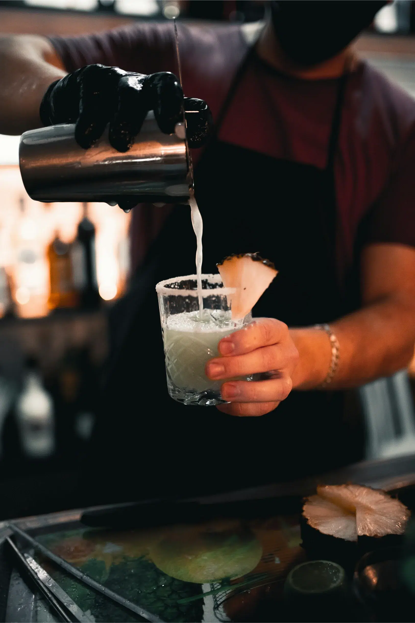 Bartender pouring cocktail into glass with pineapple slice.