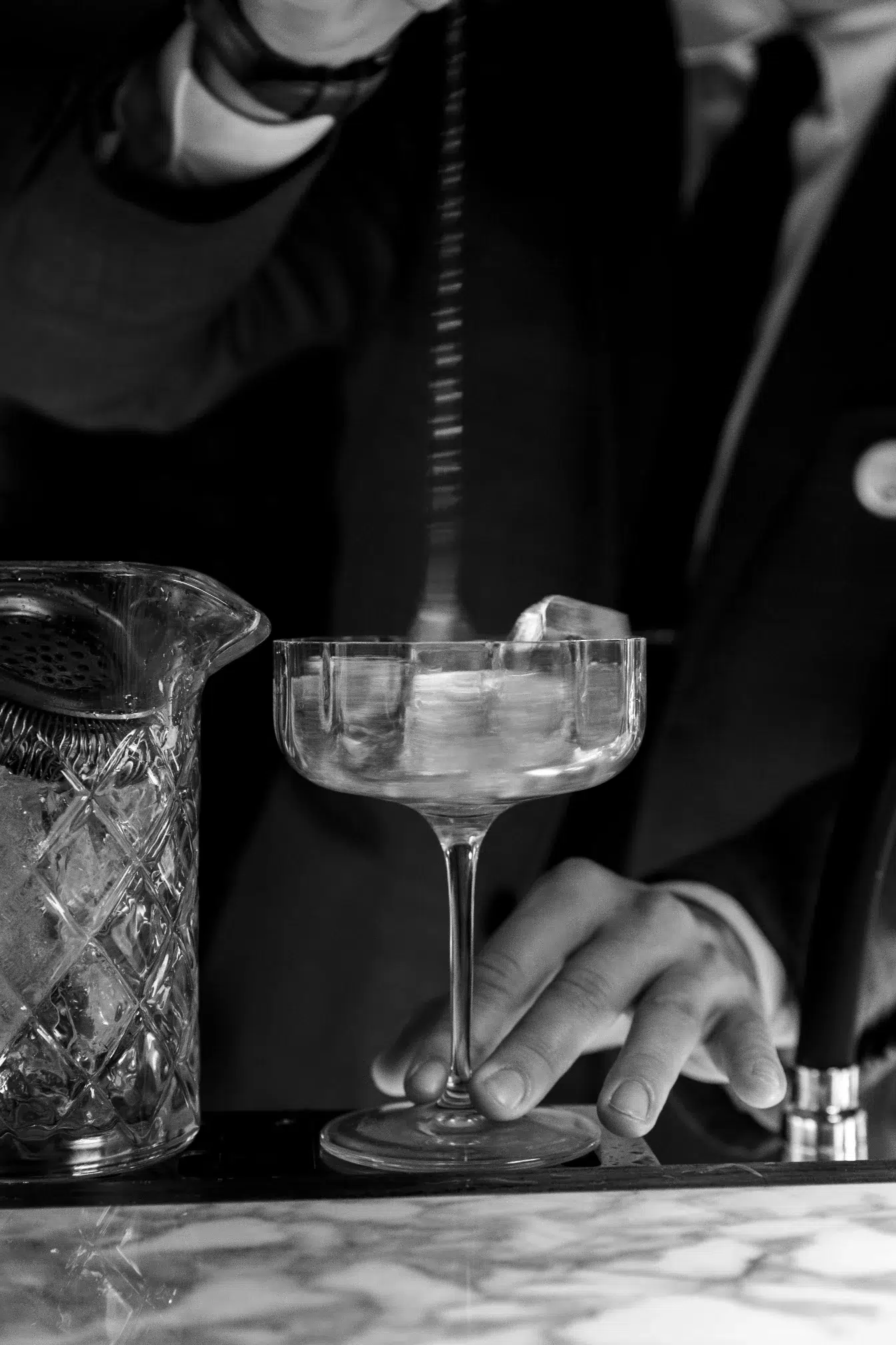 Bartender stirring drink with ice in cocktail glass.