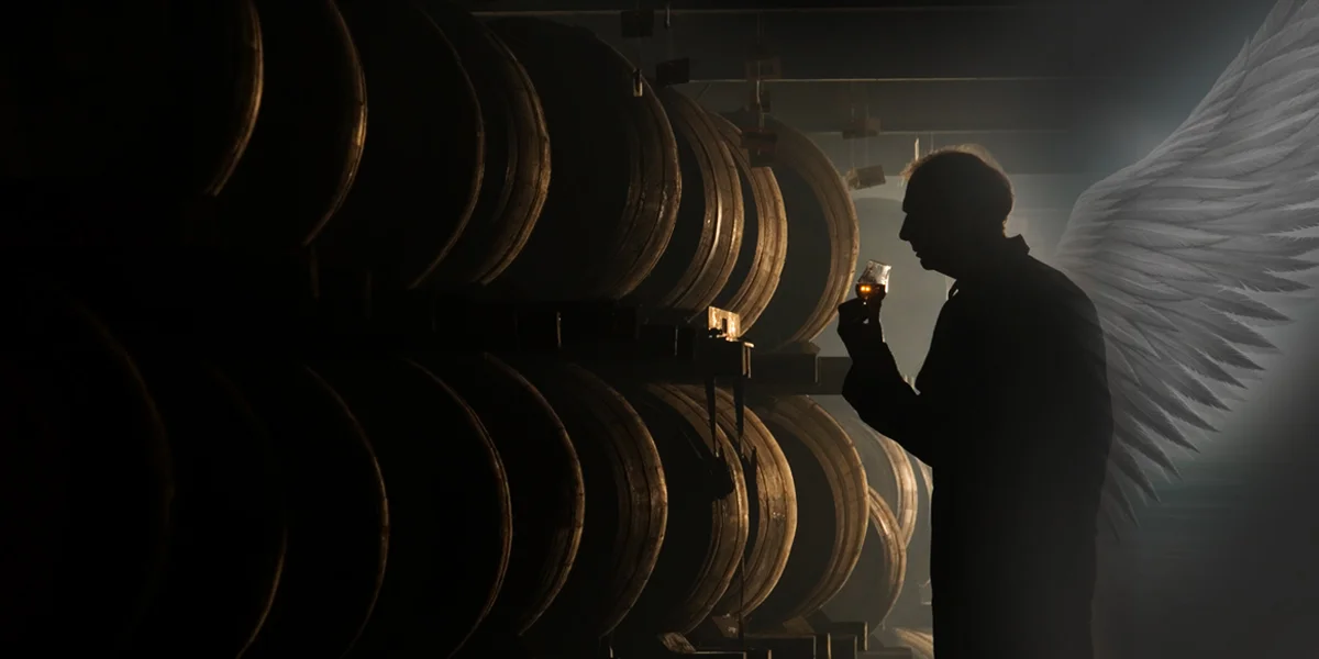 Person with angel wings tasting whisky in barrel warehouse